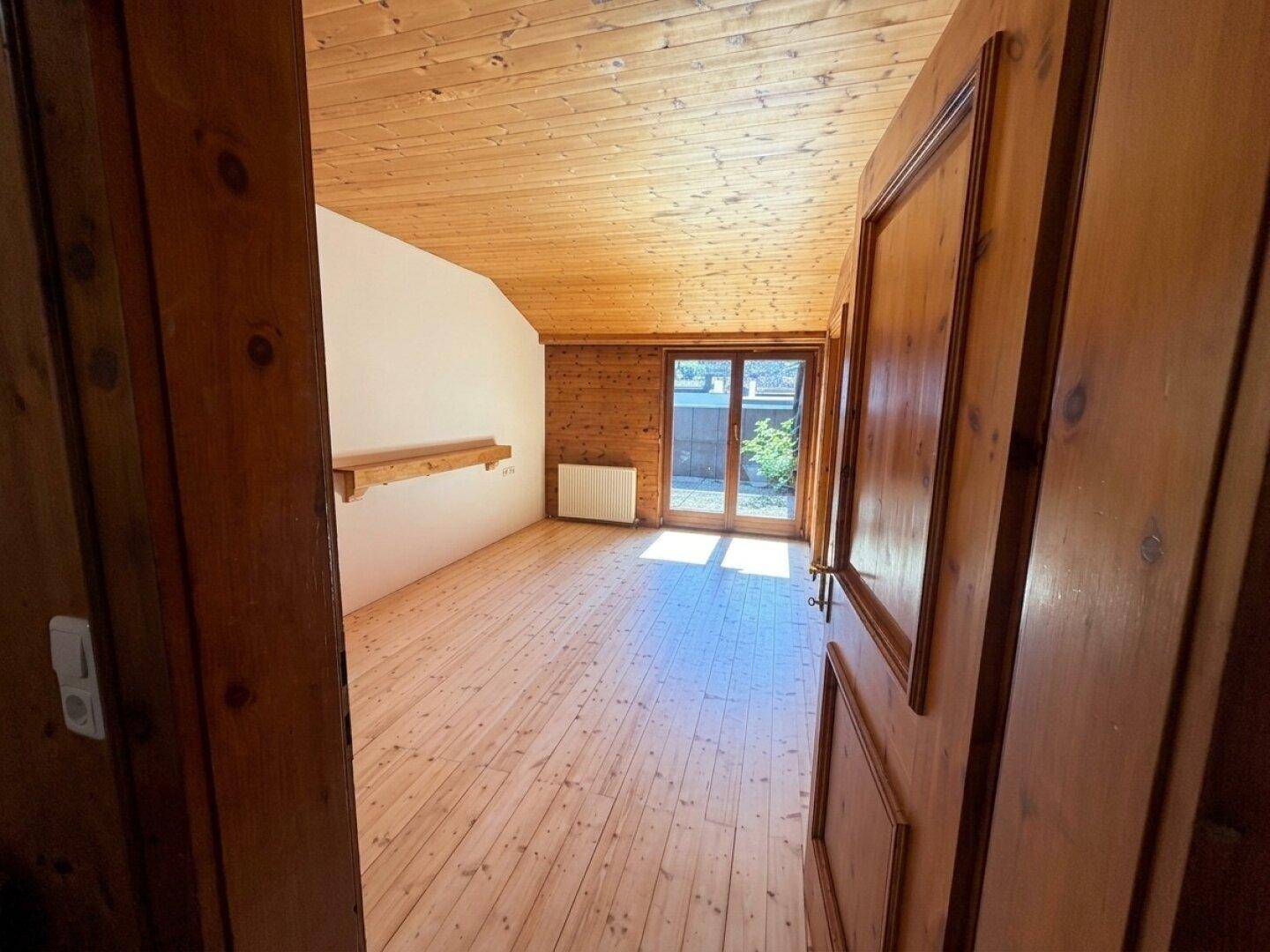 Heller Raum mit Holzdielenboden, einer Holzwand und Zugang zu einem Außenbereich.