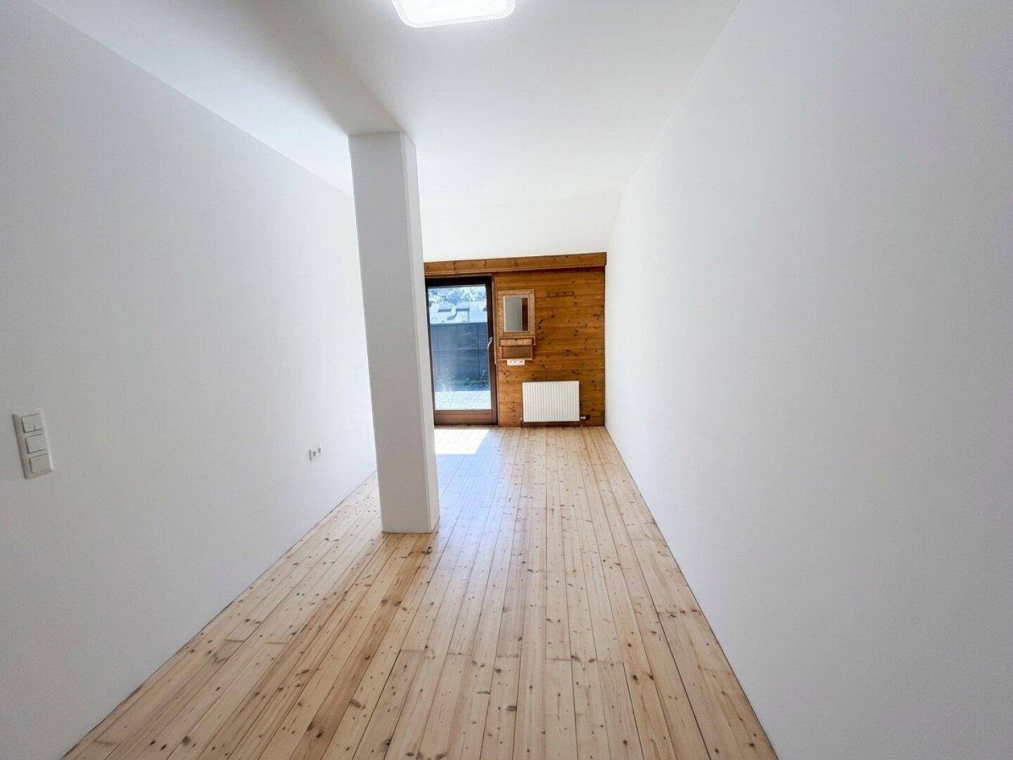 Heller Flur mit Holzdielenboden, weißen Wänden und einem Holzelement mit Spiegel.