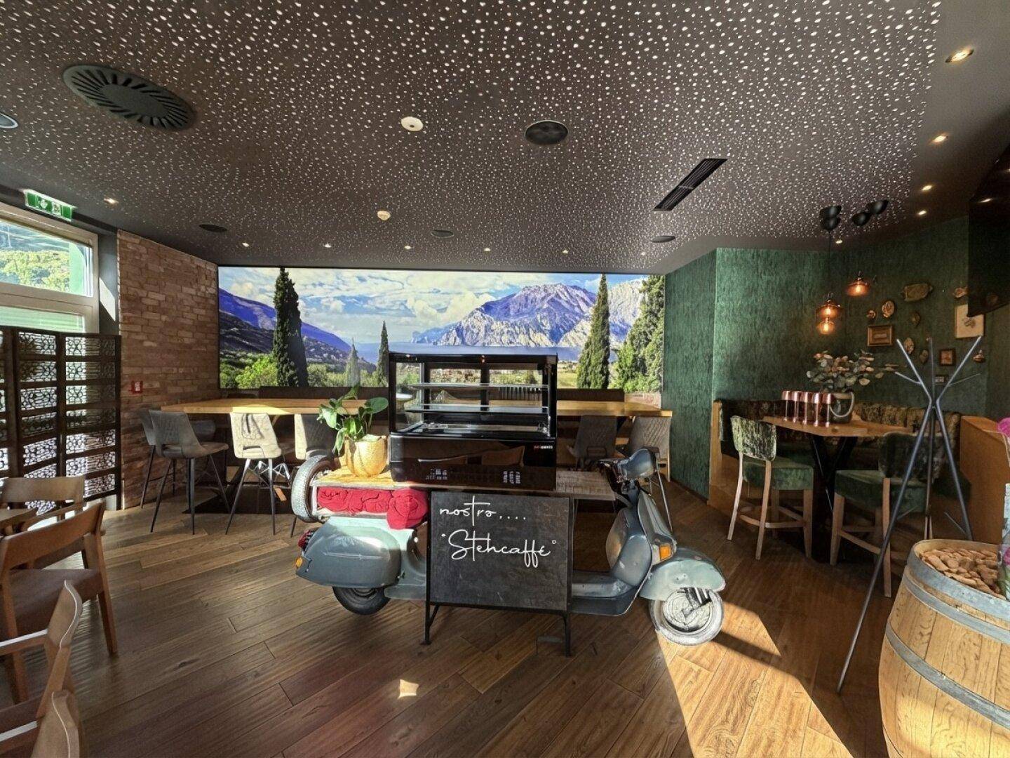 Moderner Restaurantbereich mit Holzboden, einer Vespa als Dekoration und einer Wandtapete mit italienischer Landschaft.