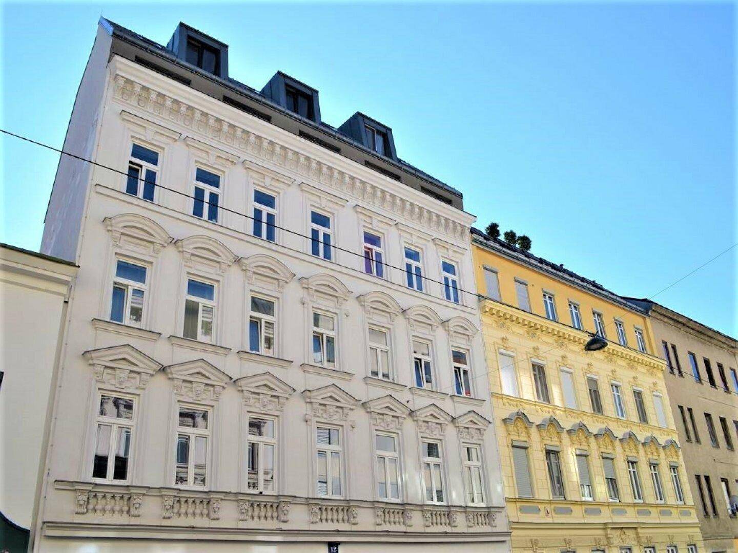 Historische Fassade eines Mehrfamilienhauses mit reich verzierten Fenstern und Dachgauben.