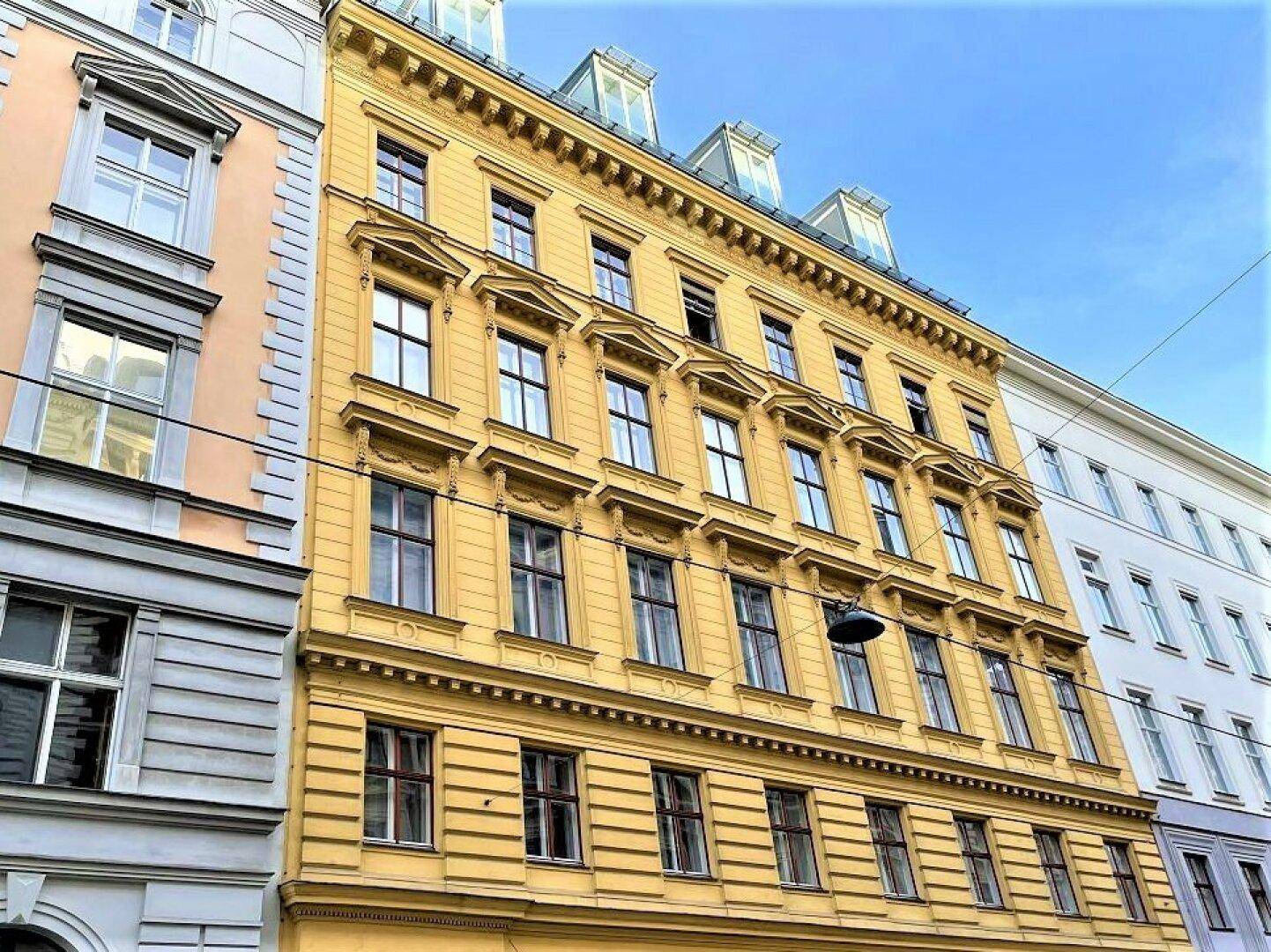 Historische Fassade eines Mehrfamilienhauses in Gelb mit vielen Fenstern und klassischen Verzierungen.