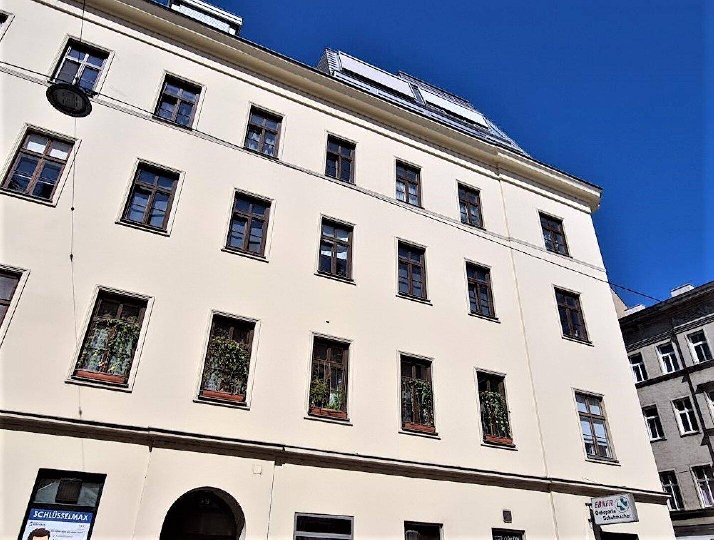 Fassade eines mehrstöckigen Gebäudes mit vielen Fenstern und einem klaren blauen Himmel im Hintergrund.