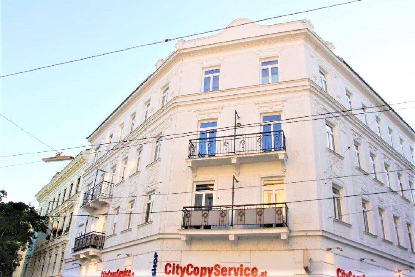 Elegantes Eckgebäude mit weißer Fassade, verzierten Balkonen und großen Fenstern unter klarem Himmel.