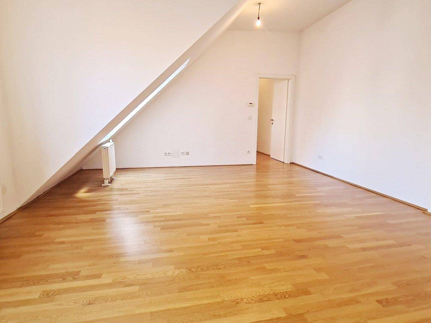 Geräumiger Wohnraum mit Holzboden und Dachschräge, ideal für individuelle Gestaltung.