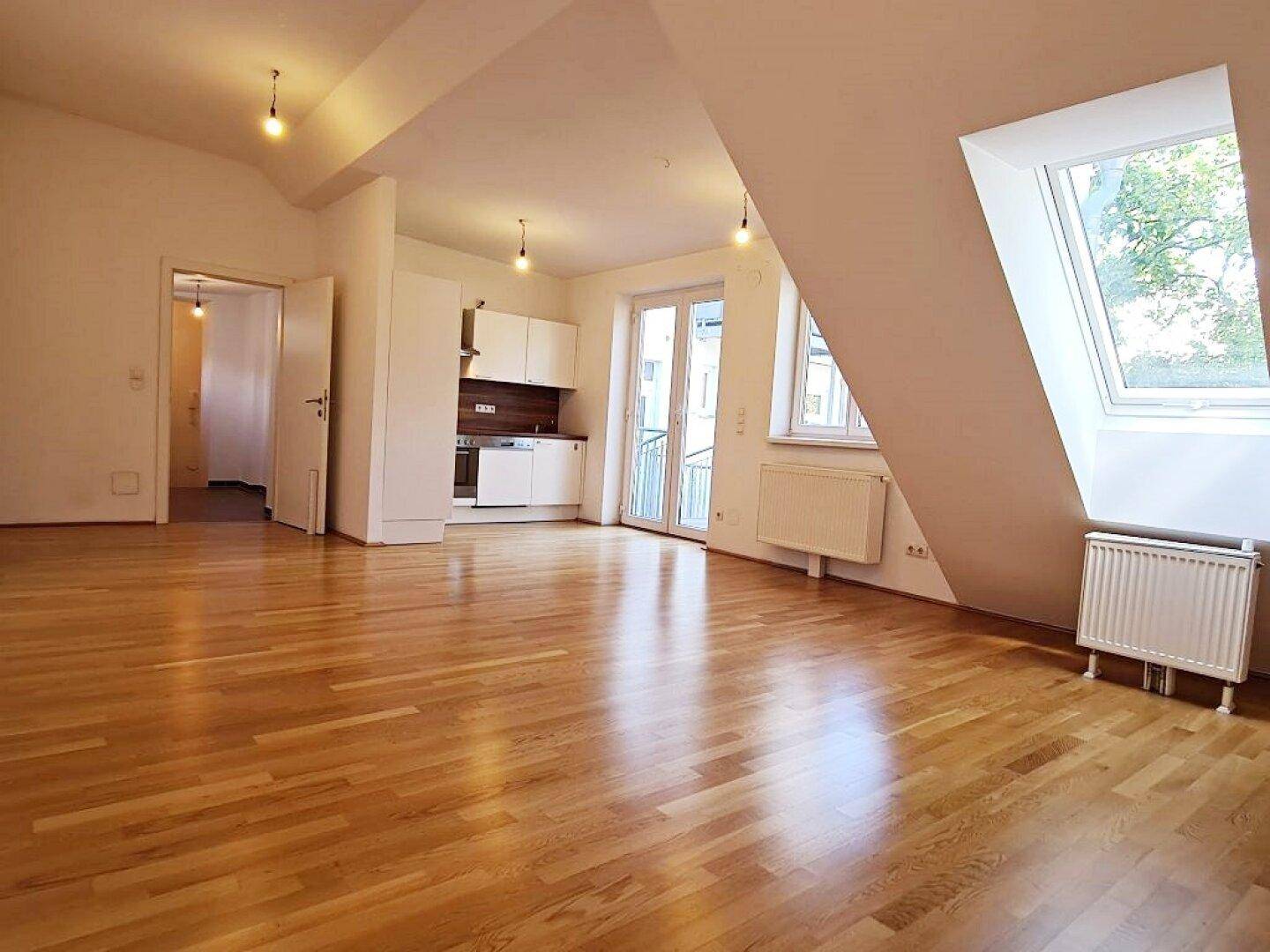 Heller Wohnbereich mit Holzboden, Dachschrägen und integrierter Küchenzeile.
