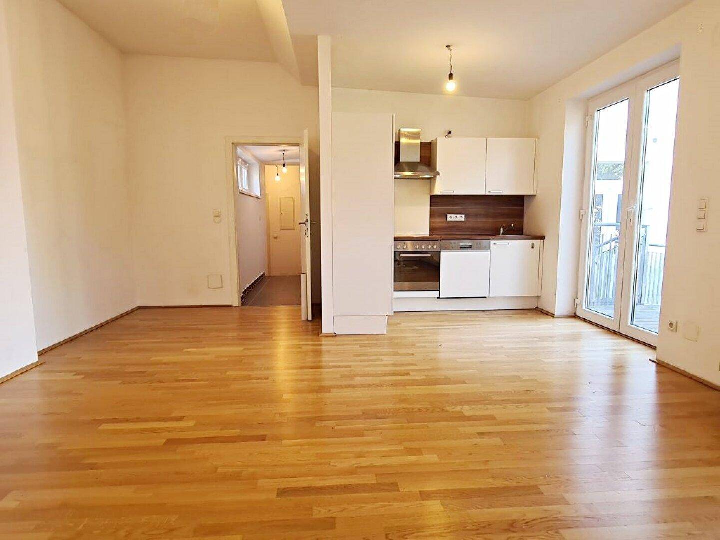 Offener Wohnbereich mit Holzboden, moderner Küchenzeile und Zugang zum Balkon.