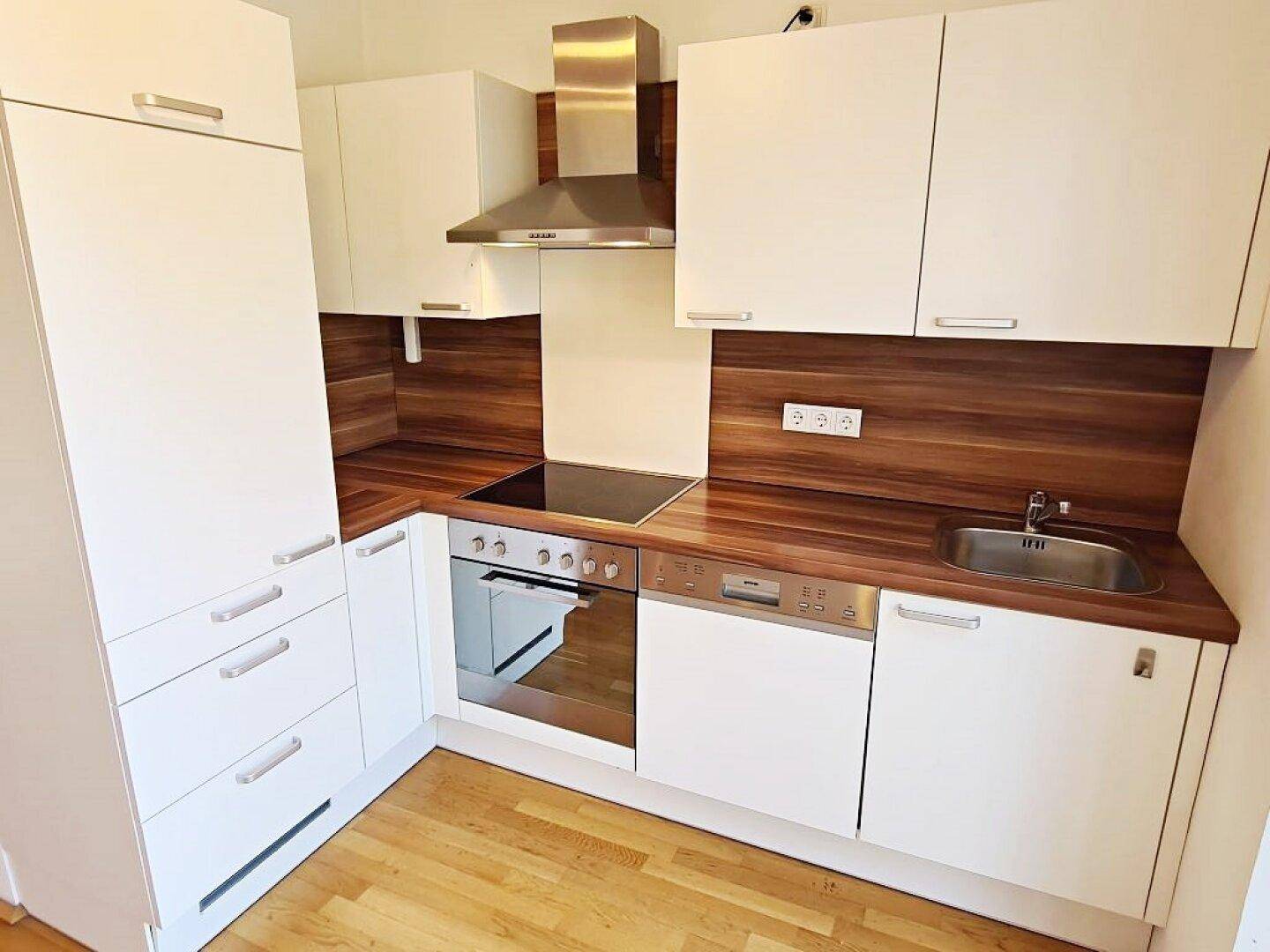 Kompakte Küchenzeile mit weißen Fronten, Holzdetails und Edelstahlgeräten.