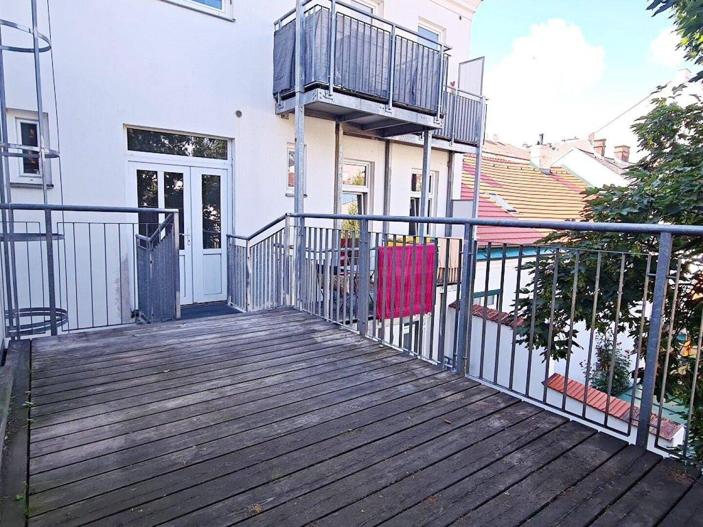 Großer Balkon mit Holzdielen und Metallgeländer, bietet Platz für Entspannung im Freien.