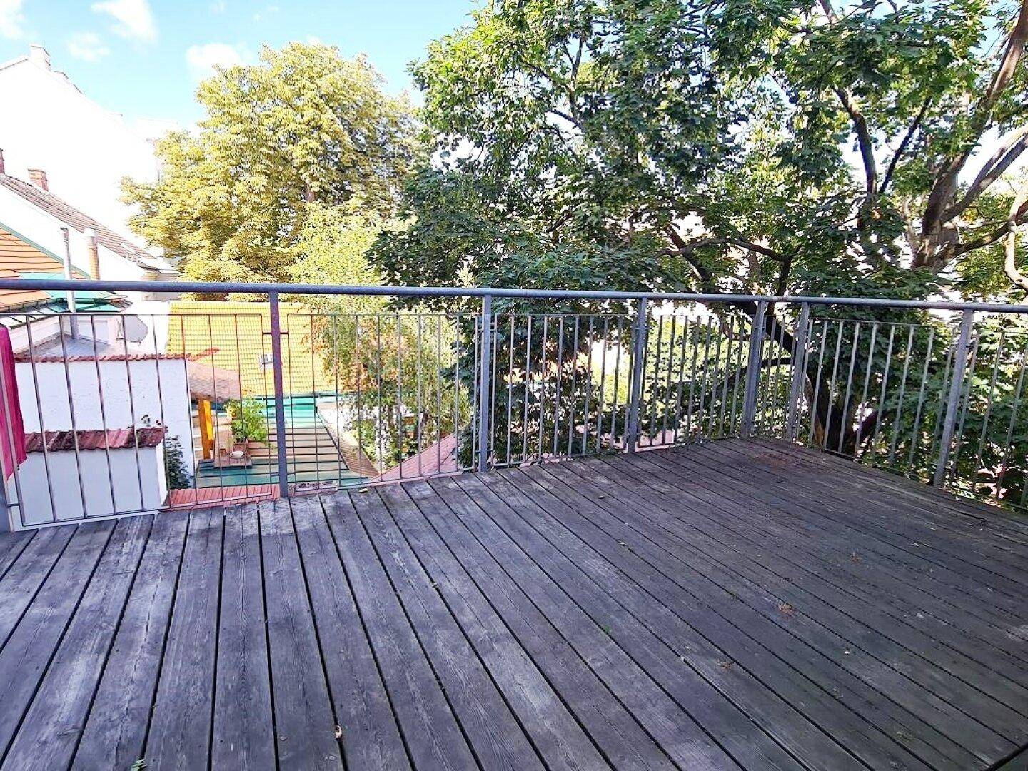 Balkon mit Holzboden und Blick auf einen Gartenbereich mit Pool.