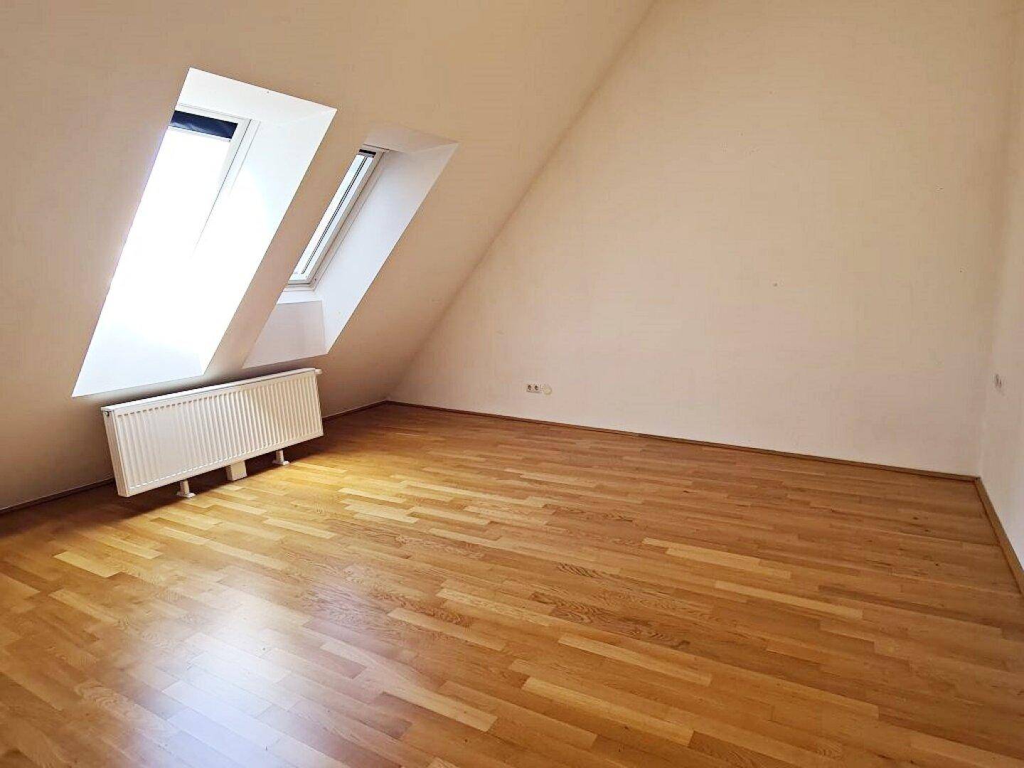Helles Zimmer mit Holzboden, Dachschrägen und zwei Dachfenstern für viel Licht.