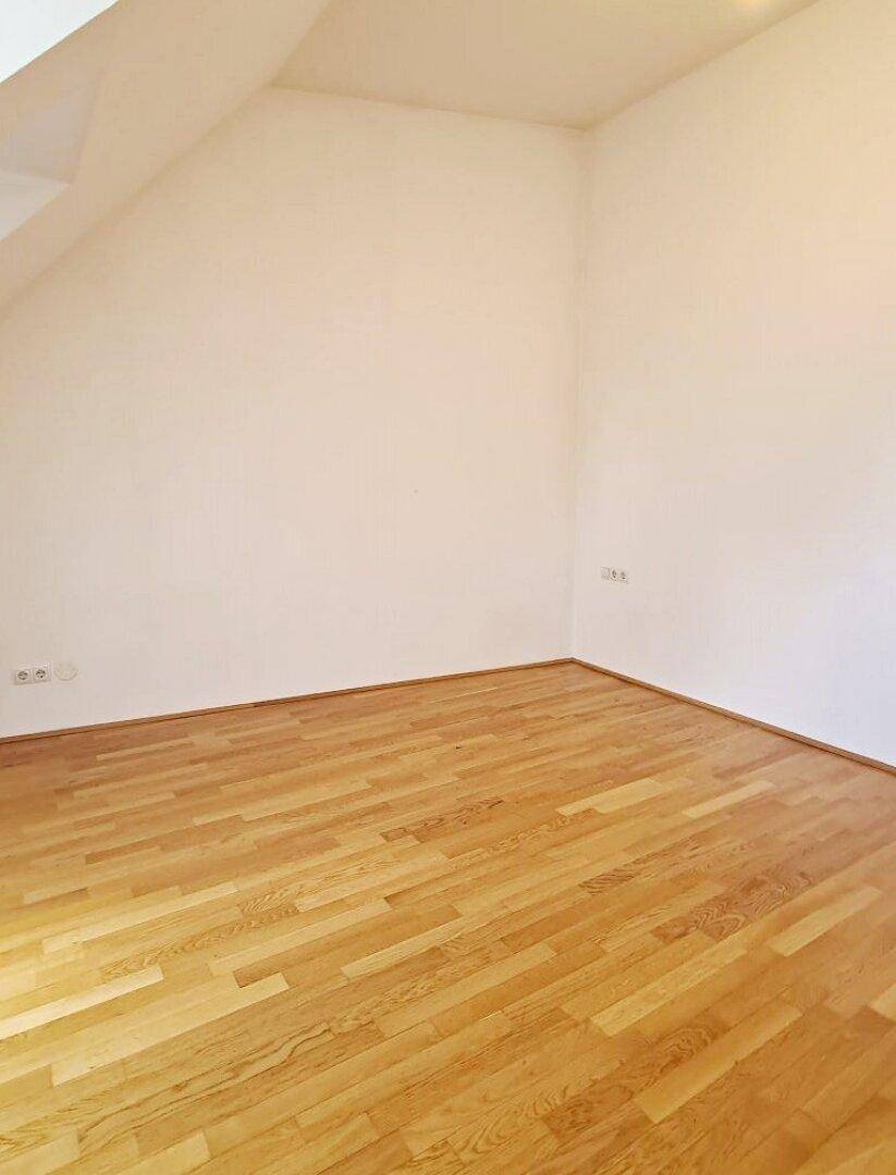 Geräumiges Zimmer mit Holzboden und weißen Wänden, bereit zur individuellen Gestaltung.