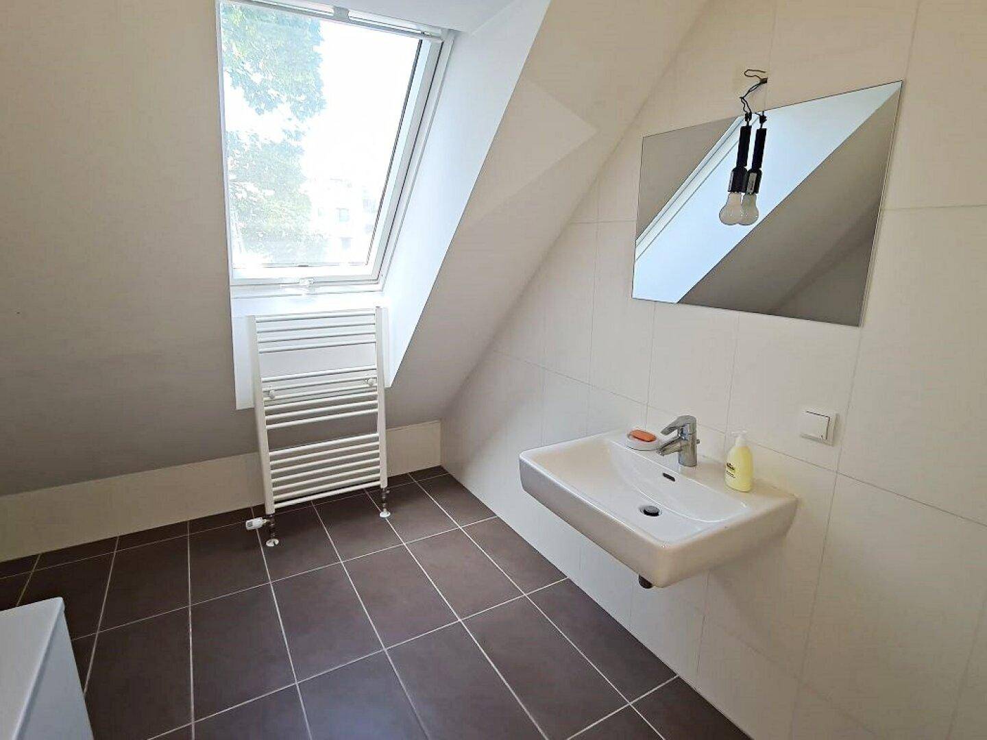 Modernes Badezimmer mit Dachfenster, Hänge-Waschbecken und braunen Fliesen.