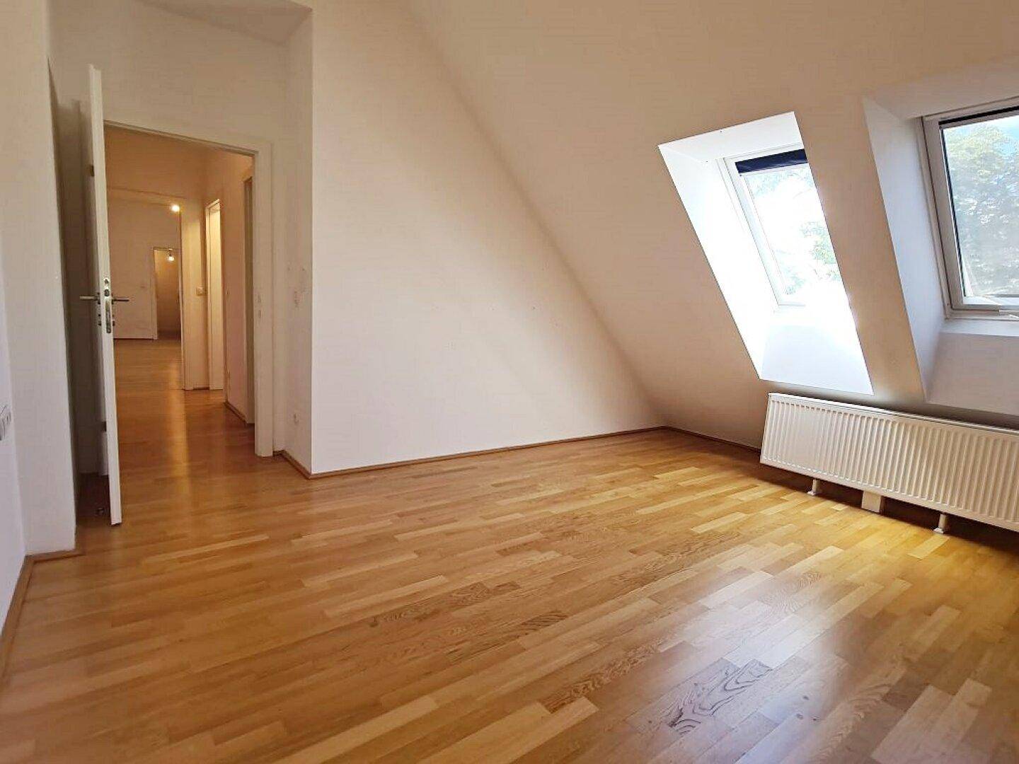 Geräumiges Zimmer mit Holzboden, Dachschräge und Fenster mit Blick ins Grüne.