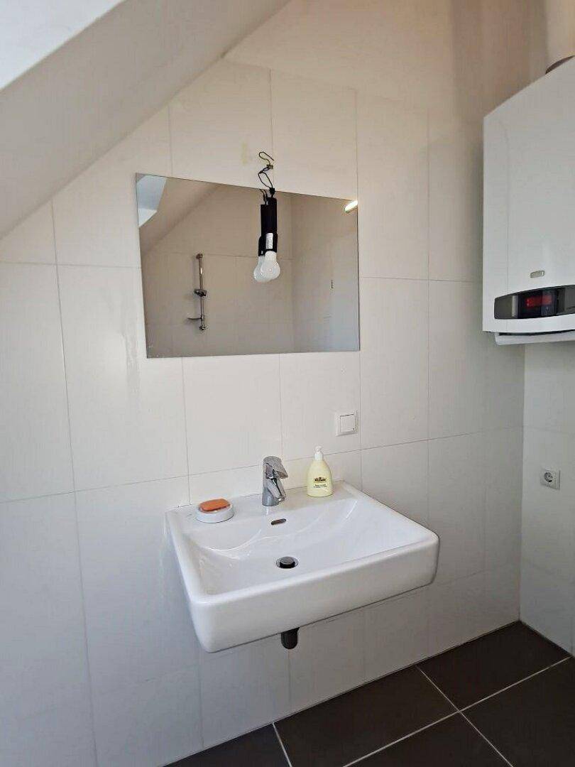 Modernes Badezimmer mit Waschbecken, Spiegel und schrägen Wänden unter dem Dach.