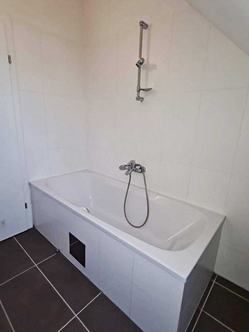 Badezimmer mit Badewanne, Duscharmatur und braunen Bodenfliesen unter Dachschräge.