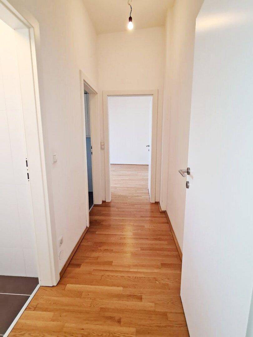 Heller Flur mit Holzparkettboden und Zugang zu weiteren Zimmern der Wohnung.