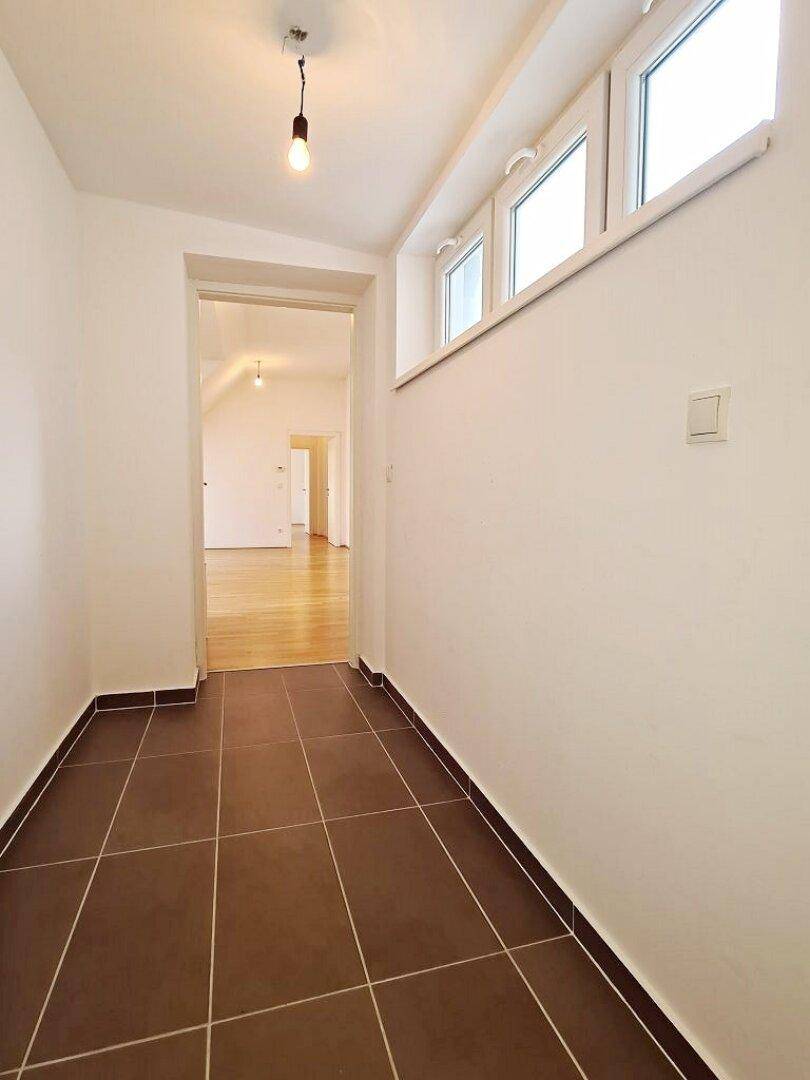Eingangsbereich mit Fliesenboden, hohen Fenstern und Blick in den Wohnbereich.