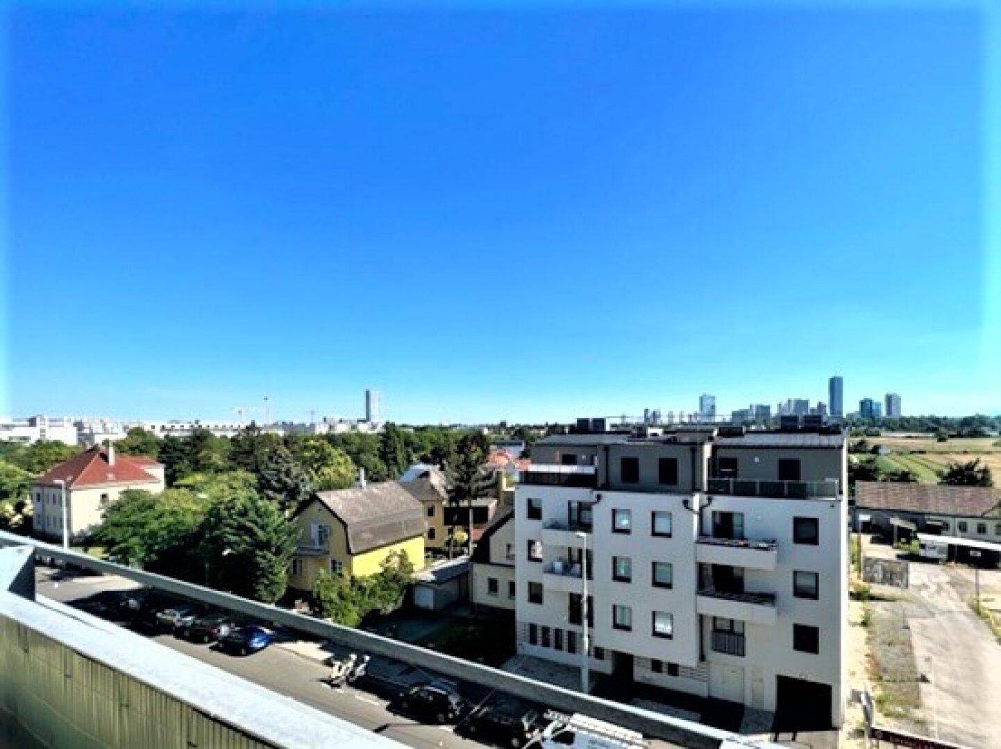 Weitläufiger Blick über eine Wohnsiedlung mit modernen Gebäuden und der Stadt im Hintergrund.