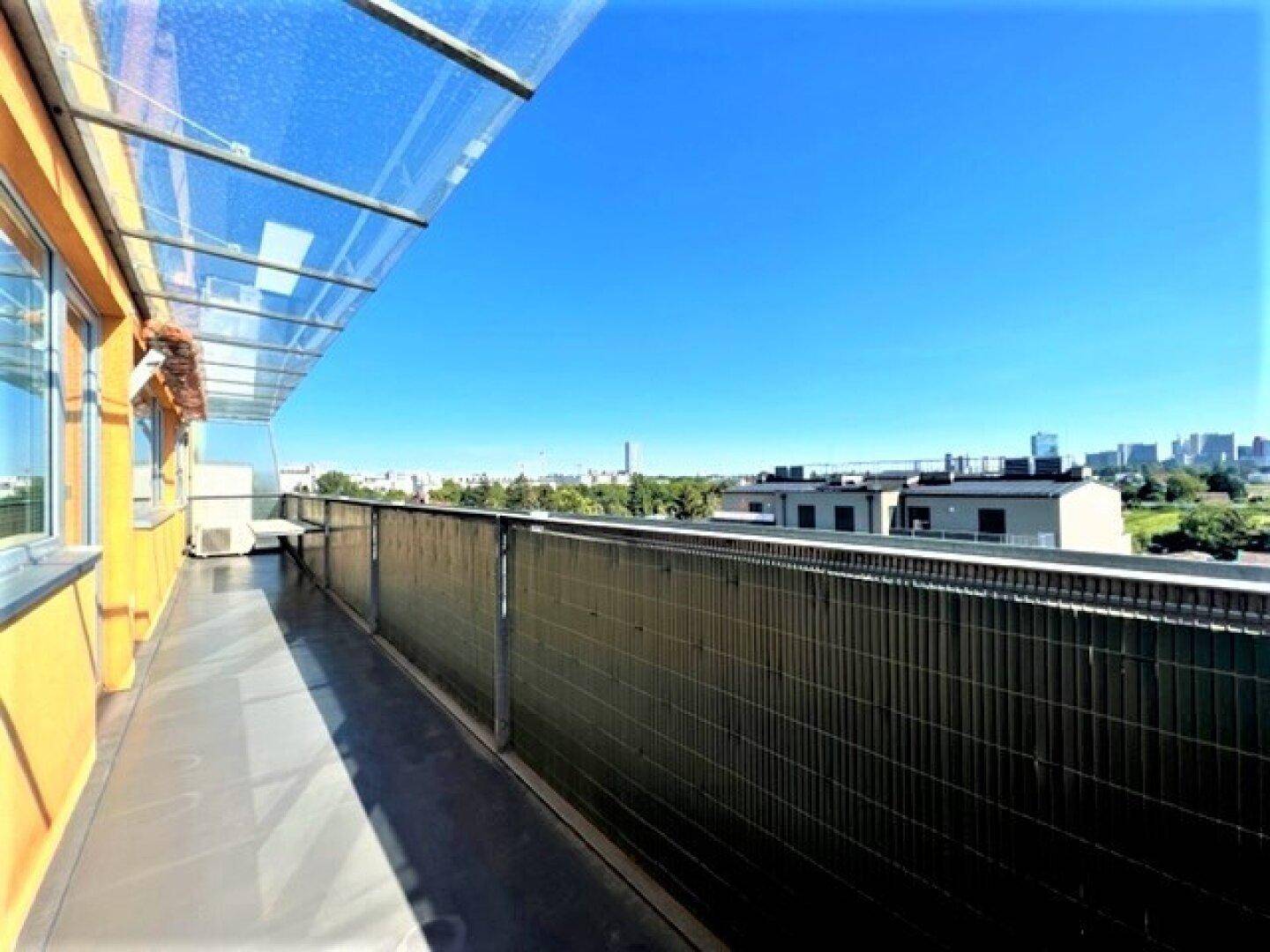 Langer Balkon mit Glasüberdachung und weitem Blick über die Stadt und Wohngebäude.