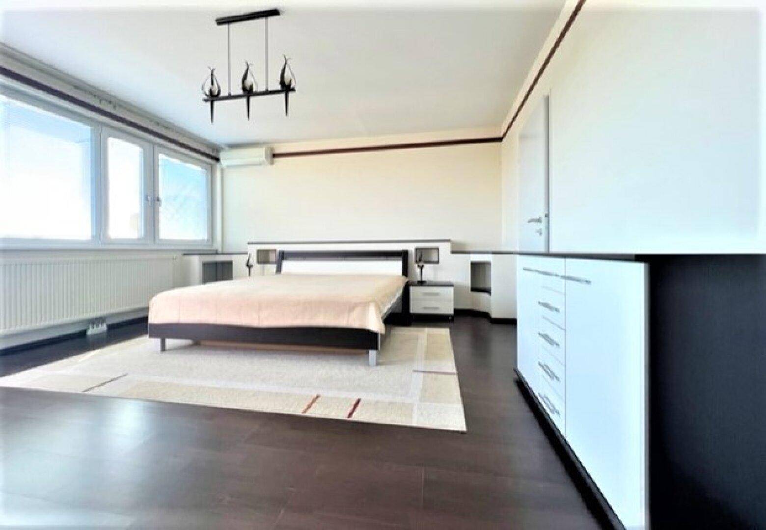 Geräumiges Schlafzimmer mit dunklem Holzboden, Doppelbett und großen Fenstern.