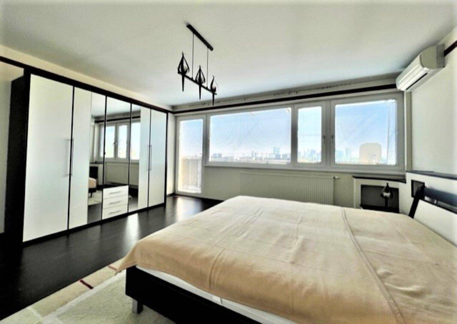 Schlafzimmer mit großem Bett, Spiegelschränken und weitem Blick durch die Fenster.