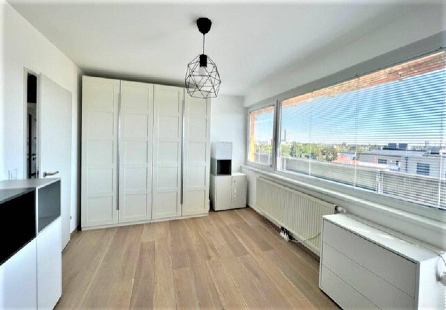 Helles Schlafzimmer mit hellem Holzboden, weißem Kleiderschrank und großen Fenstern.