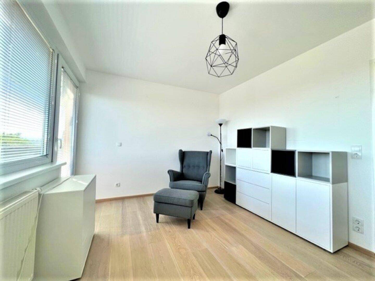 Heller Raum mit Holzboden, Sessel und modularen Regalsystemen.