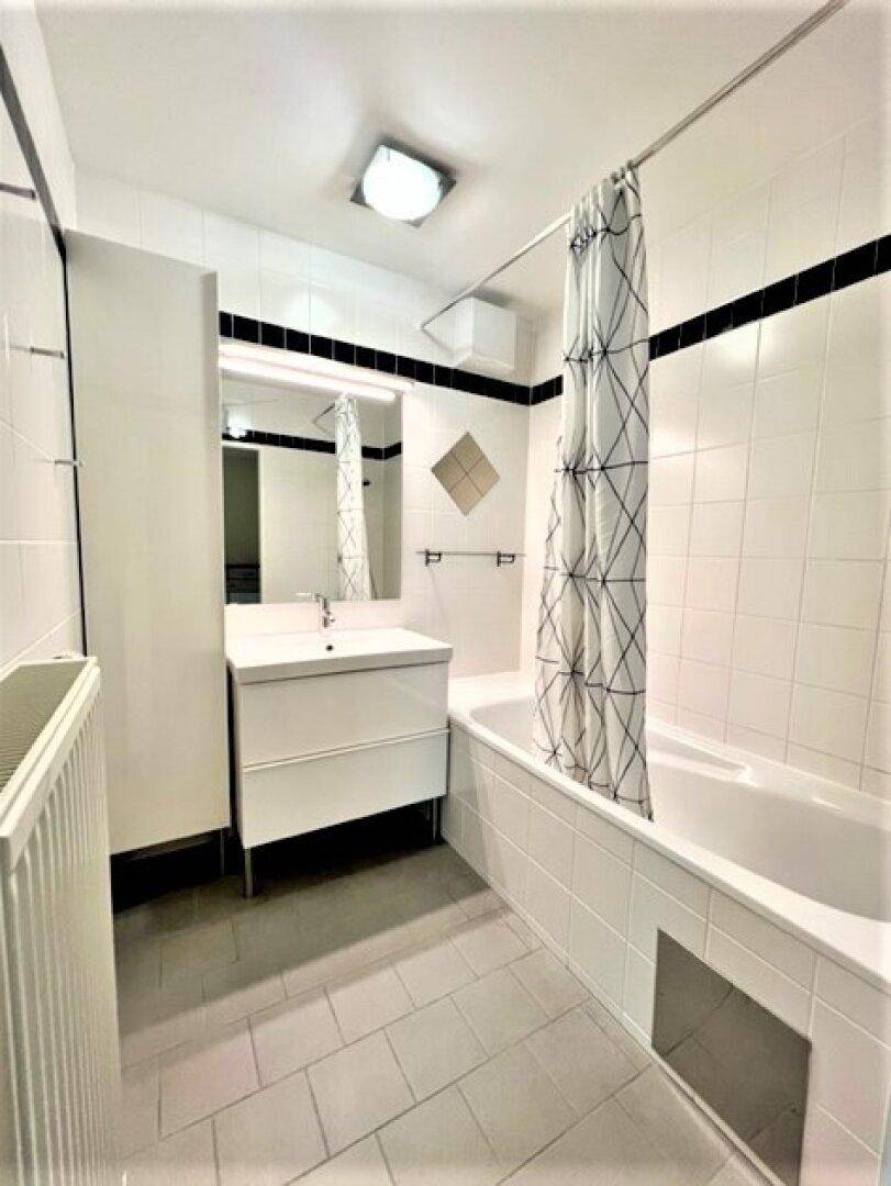 Helles Badezimmer mit Badewanne, Duschvorhang, Waschbecken und weißen Fliesen.