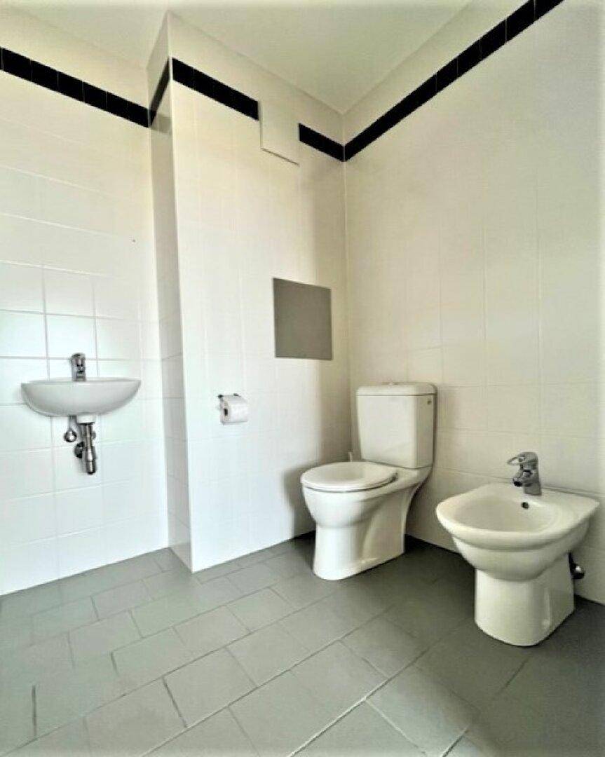 Separates WC mit Bidet, kleinem Waschbecken und grauen Bodenfliesen.