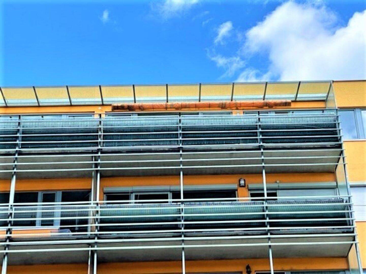 Fassade eines Gebäudes mit mehreren Balkonen, die mit Metallgeländern und Sichtschutz ausgestattet sind.