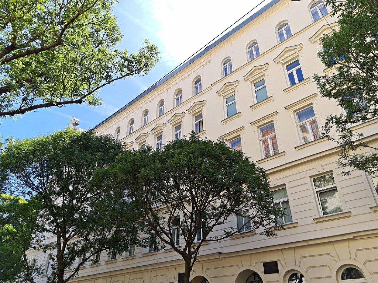 Gebäudefassade mit klassischer Architektur, umgeben von Bäumen, die einen grünen Ausblick bieten.