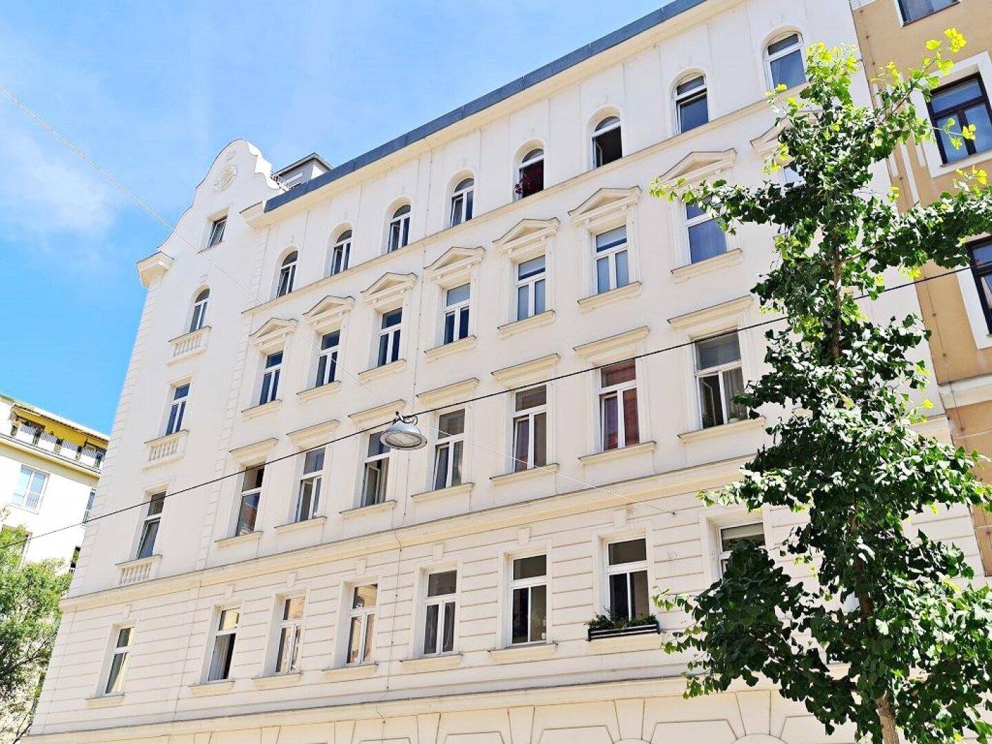 Klassische Fassade eines Mehrfamilienhauses mit vielen Fenstern und architektonischen Details unter blauem Himmel.