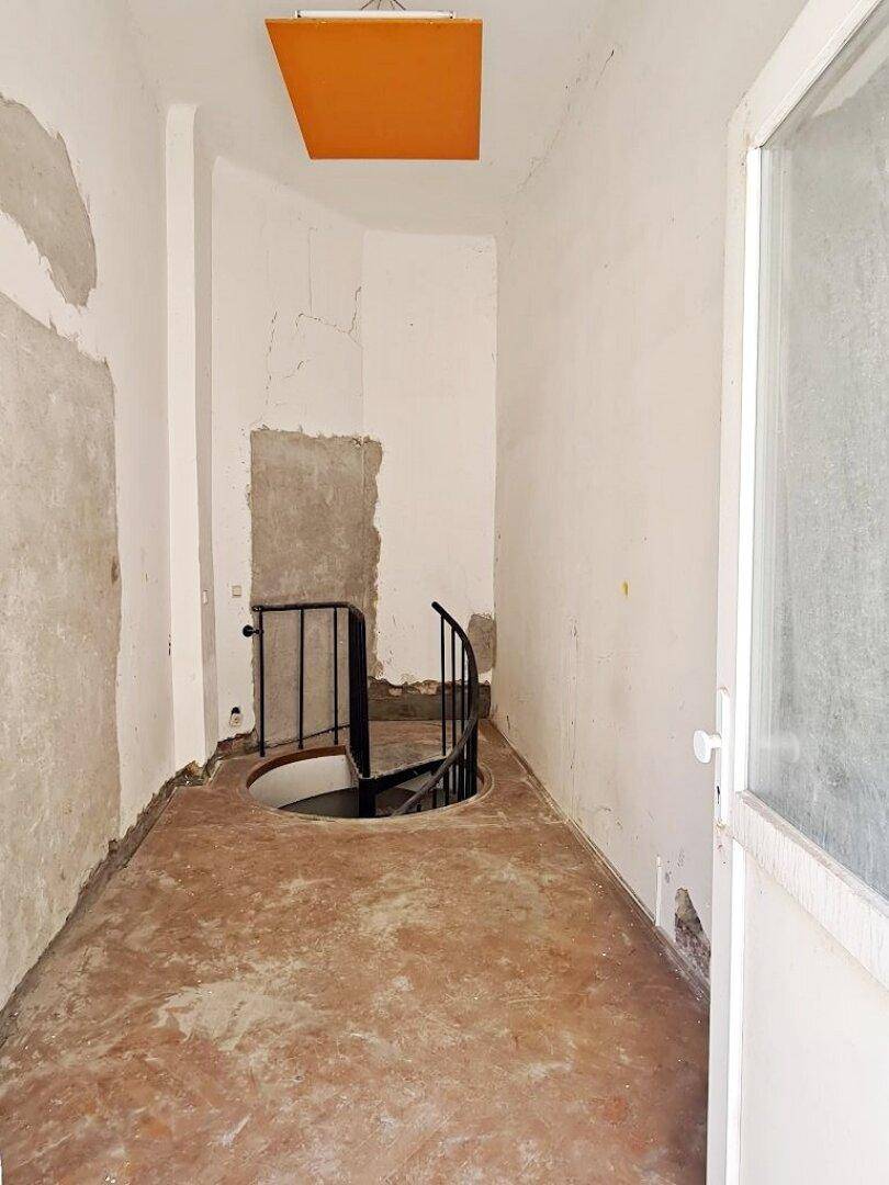 Flur mit einer Wendeltreppe, die nach unten führt, und einer orangefarbenen Deckenplatte in renovierungsbedürftigem Zustand.