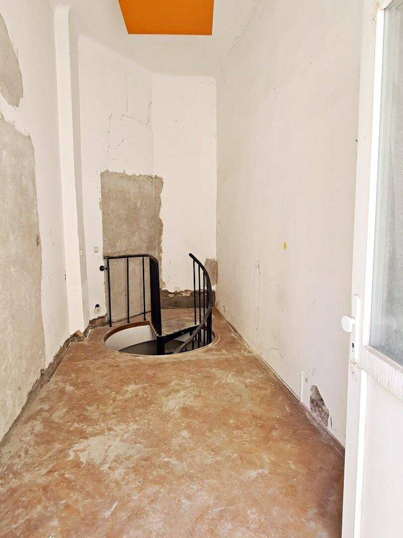 Flur mit einer Wendeltreppe, die nach unten führt, und einer orangefarbenen Deckenplatte in renovierungsbedürftigem Zustand.