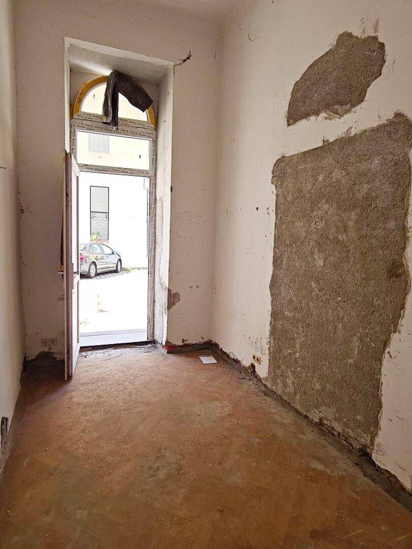 Innenraum mit offener Tür zum Außenbereich und sichtbaren Renovierungsspuren an den Wänden.