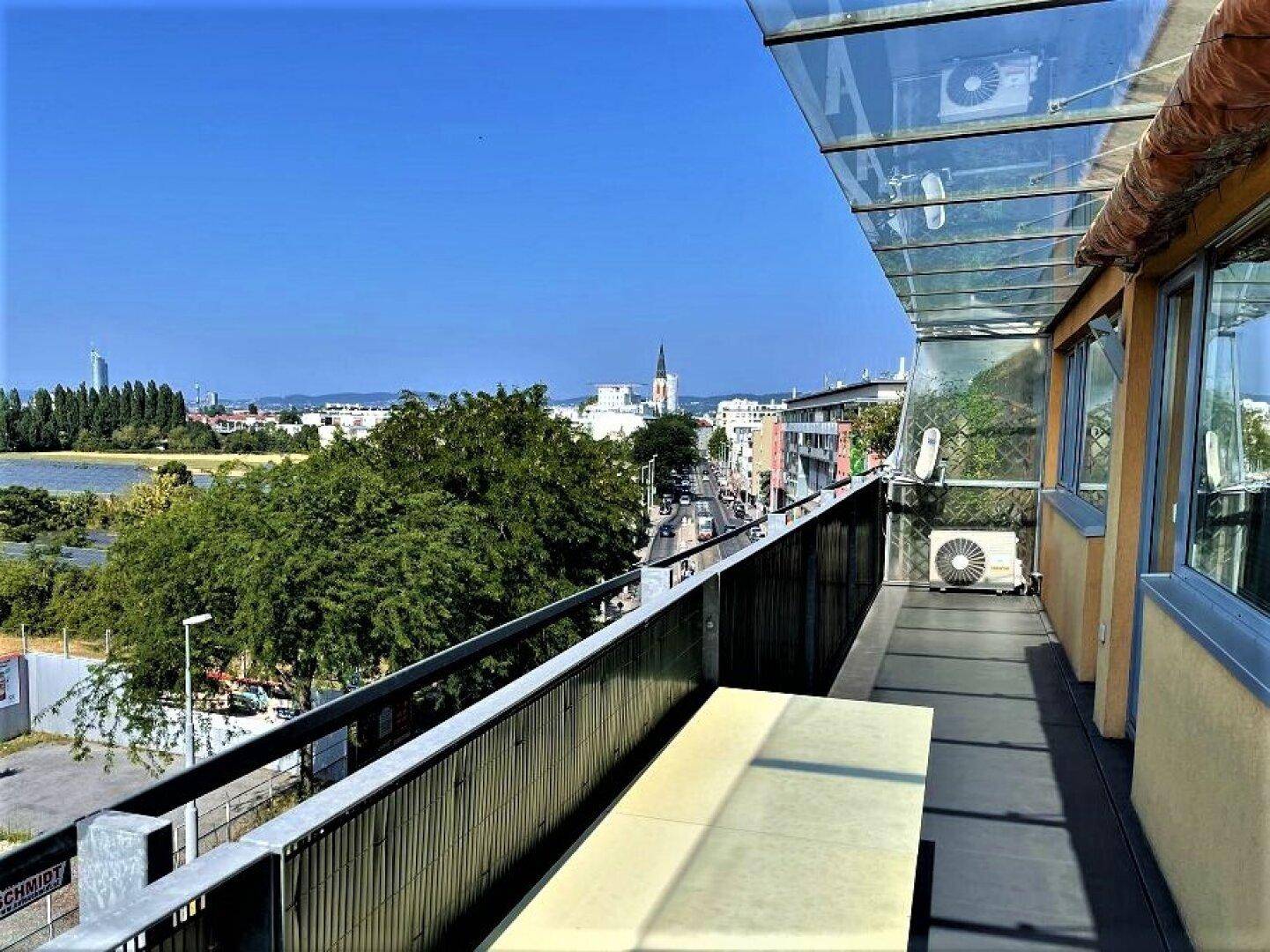 Geräumiger Balkon mit Glasdach und weitem Blick über die Stadt und einen See.