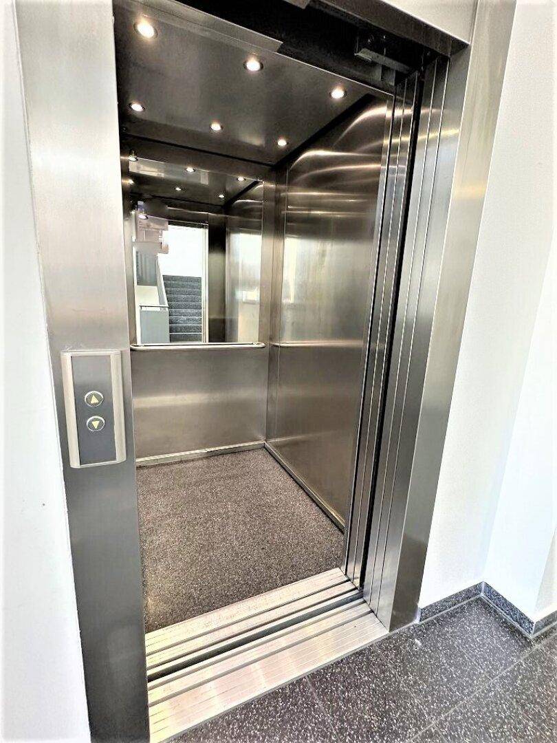 Moderner Aufzug mit Edelstahlwänden, Spiegelfläche und grauem Teppichboden.