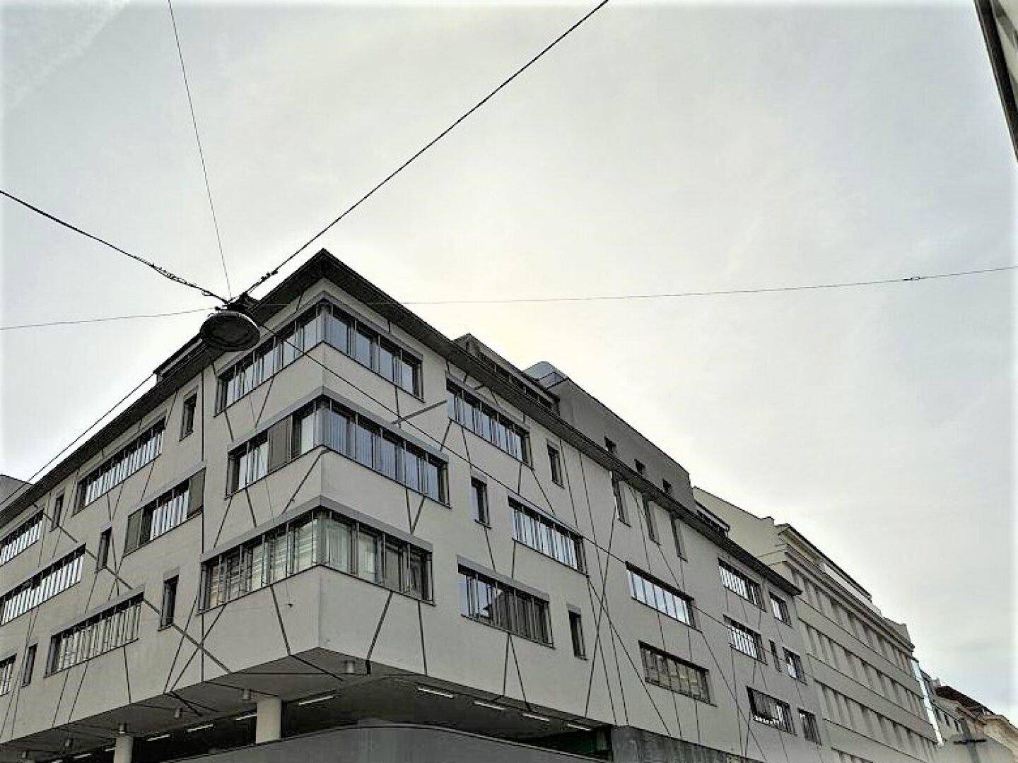 Moderne Gebäudefassade mit markanten geometrischen Mustern und großen Fensterfronten unter bewölktem Himmel.
