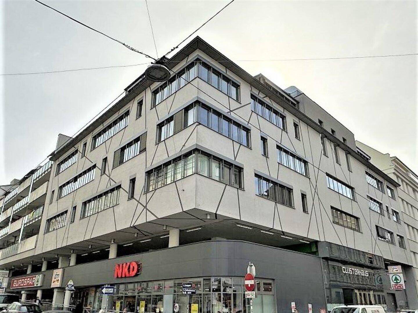 Gebäudefassade mit moderner Architektur, Einzelhandelsgeschäften im Erdgeschoss und urbaner Umgebung.