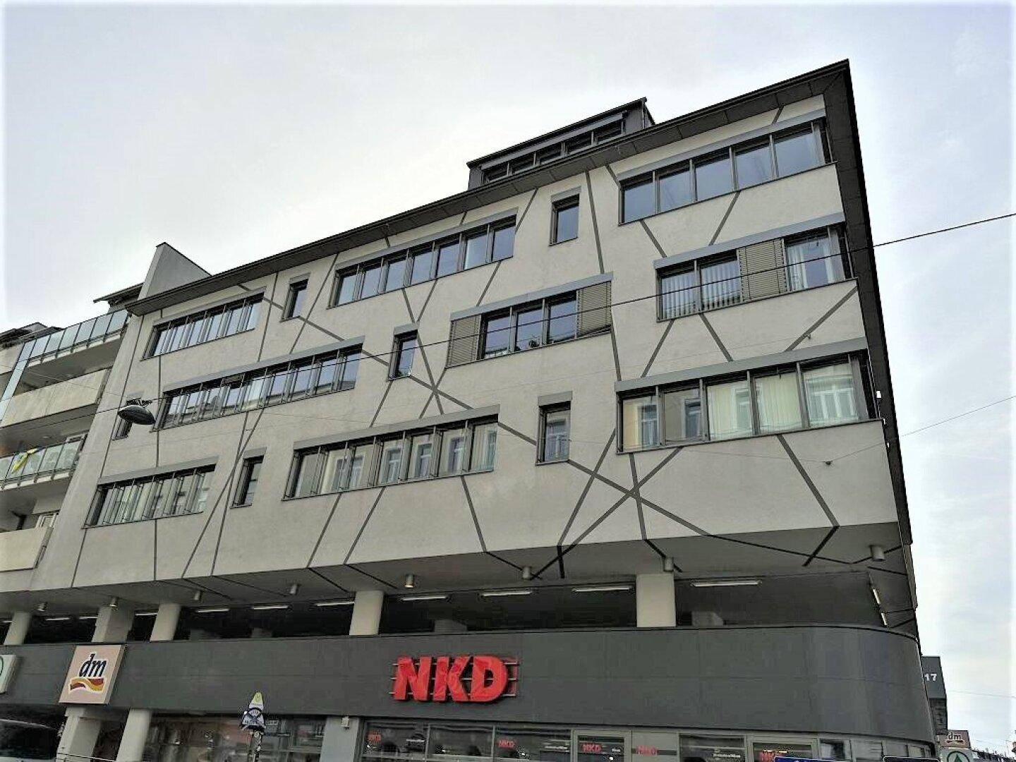 Gebäudefassade mit moderner Architektur, großen Fenstern und Einzelhandelsgeschäften im Erdgeschoss.