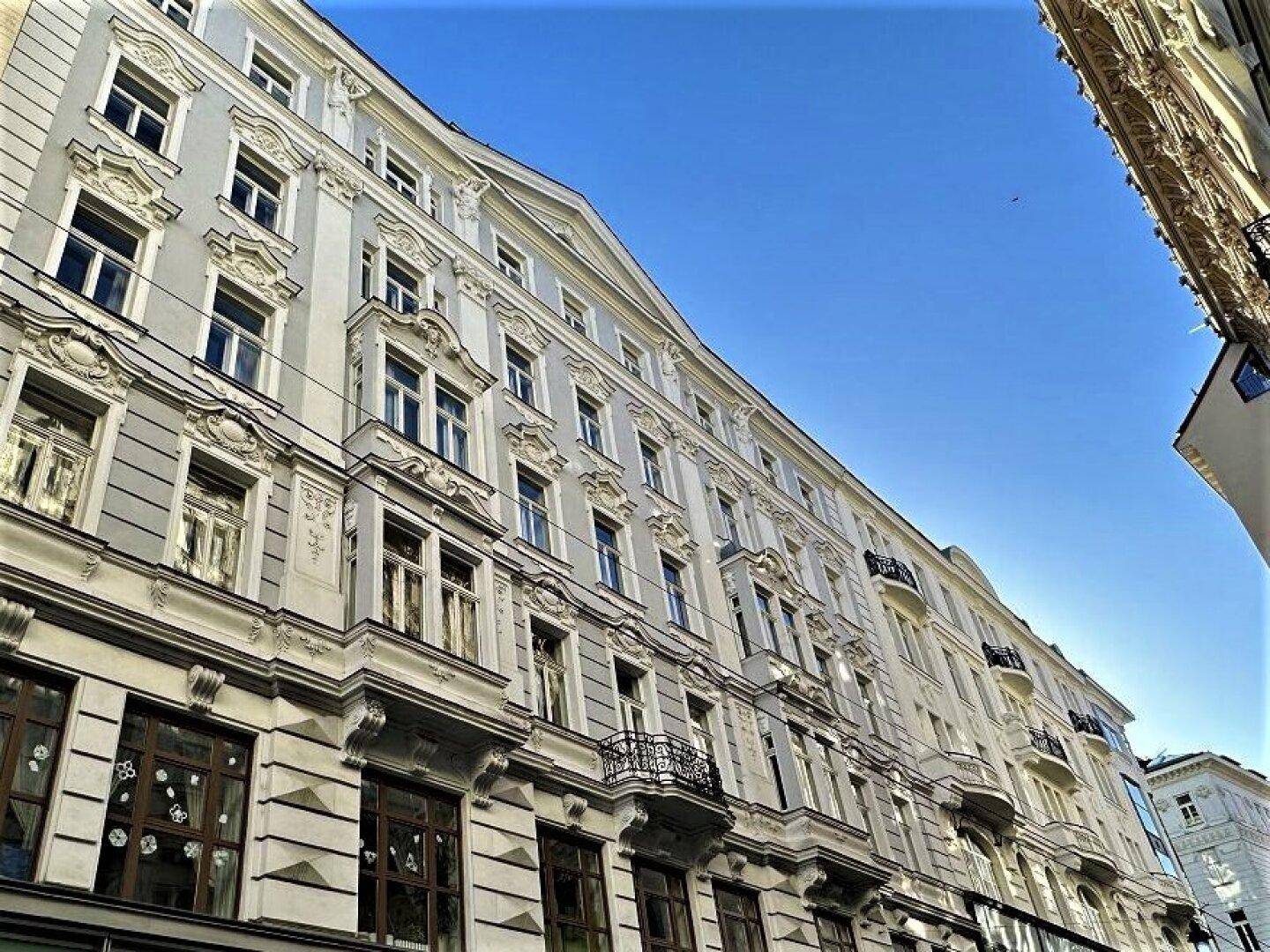 Historische Fassade eines eleganten Altbaus mit vielen Fenstern und kleinen Balkonen unter blauem Himmel.
