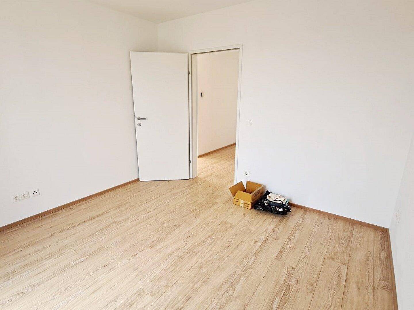 Leeres Zimmer mit Holzboden und offener Tür, bereit zur individuellen Gestaltung.