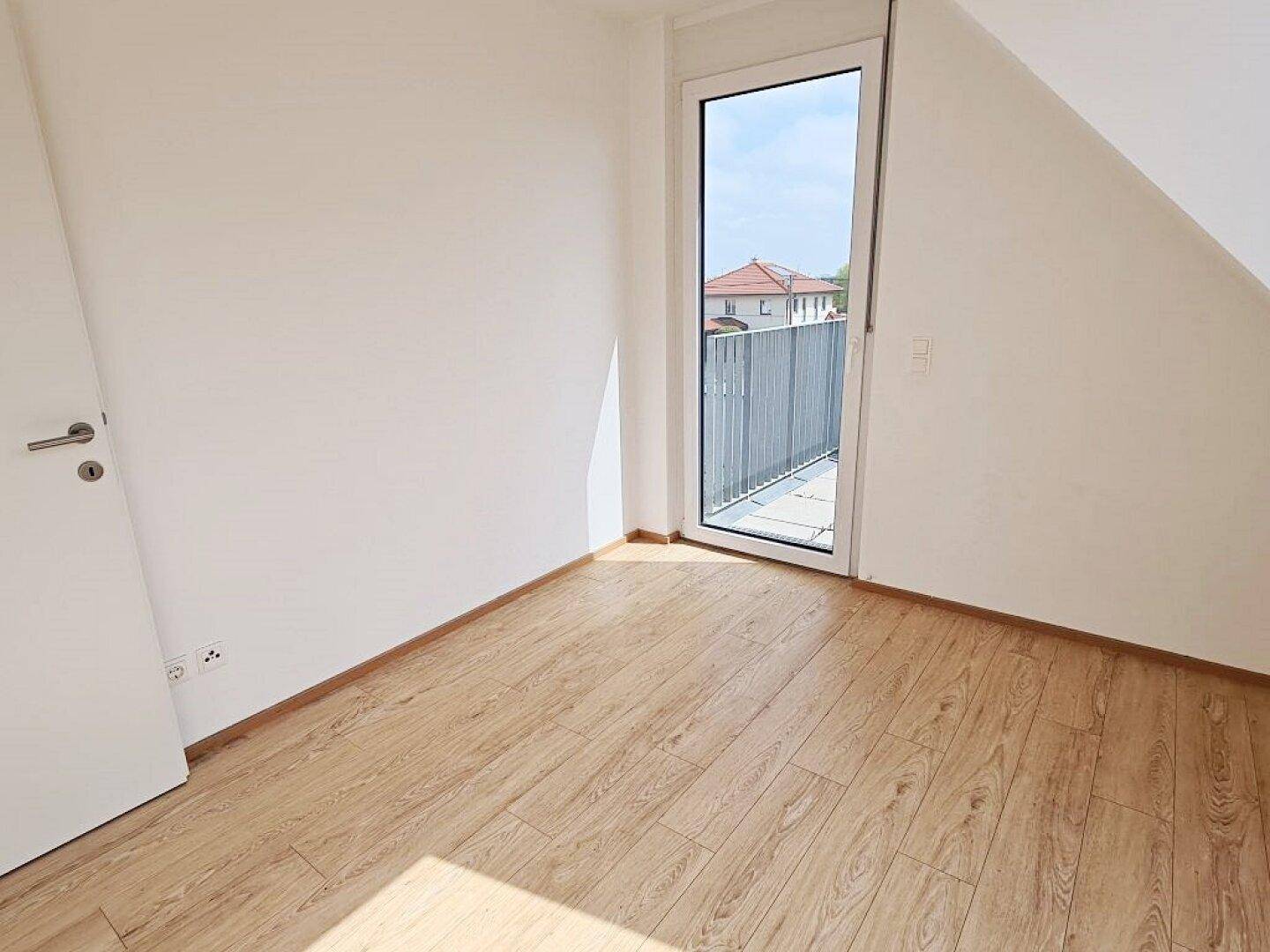 Helles Schlafzimmer mit Holzboden, Dachschräge und direktem Zugang zu einem Balkon.