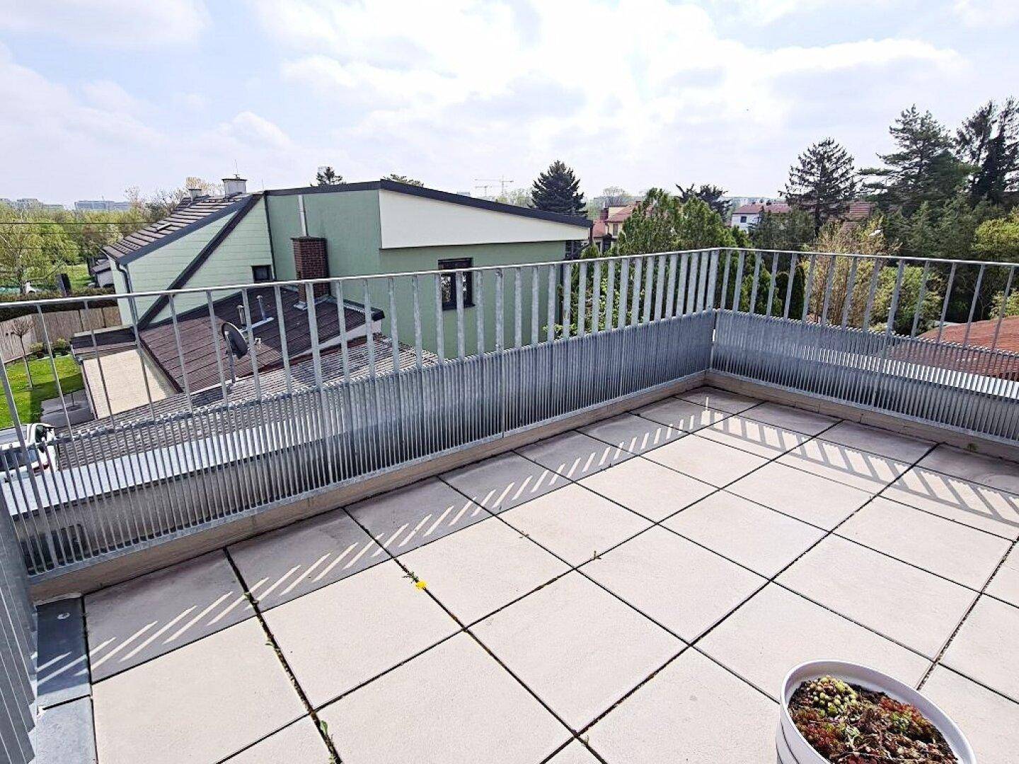 Geräumiger Balkon mit Fliesenboden und schöner Aussicht auf grüne Bäume und Nachbarhäuser.