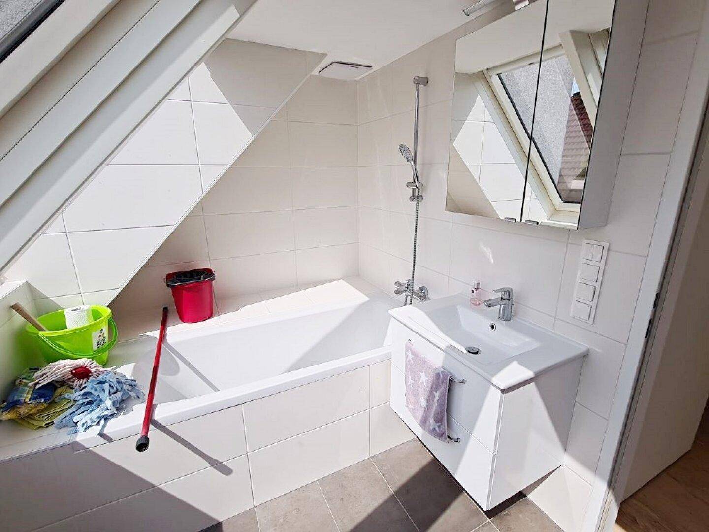 Modernes Badezimmer mit Badewanne, Waschbecken, Spiegelschrank und Dachfenster unter der Schräge.