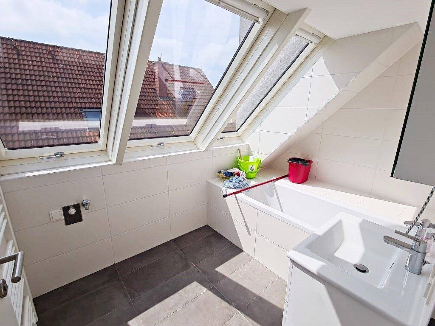 Helles Badezimmer im Dachgeschoss mit Badewanne, Waschbecken und großen Dachfenstern für viel Tageslicht.