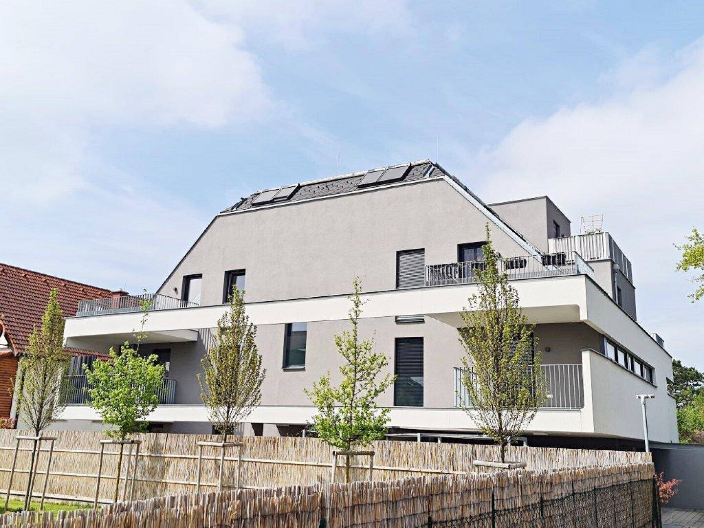 Moderne Wohnanlage mit mehreren Balkonen, schräger Dachkonstruktion und Photovoltaikanlage.