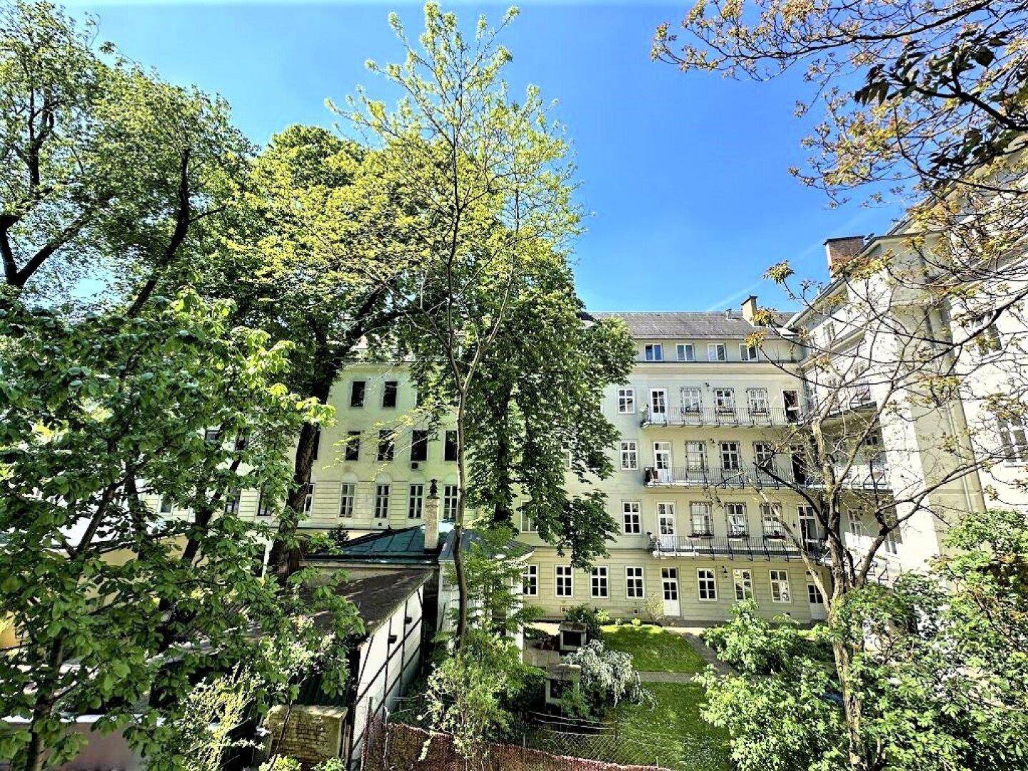 Blick auf den grünen Innenhof mit Bäumen und die Fassaden der umliegenden Gebäude.