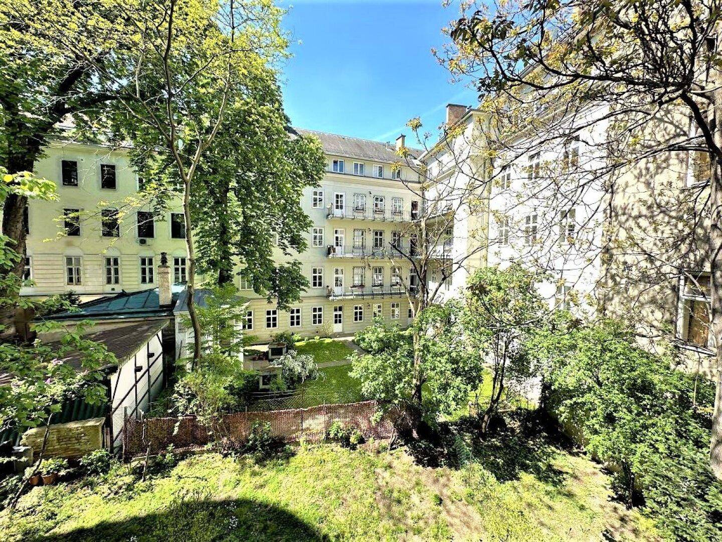 Sonnige Ansicht des grünen Innenhofs mit Bäumen und den Fassaden der umliegenden Gebäude.