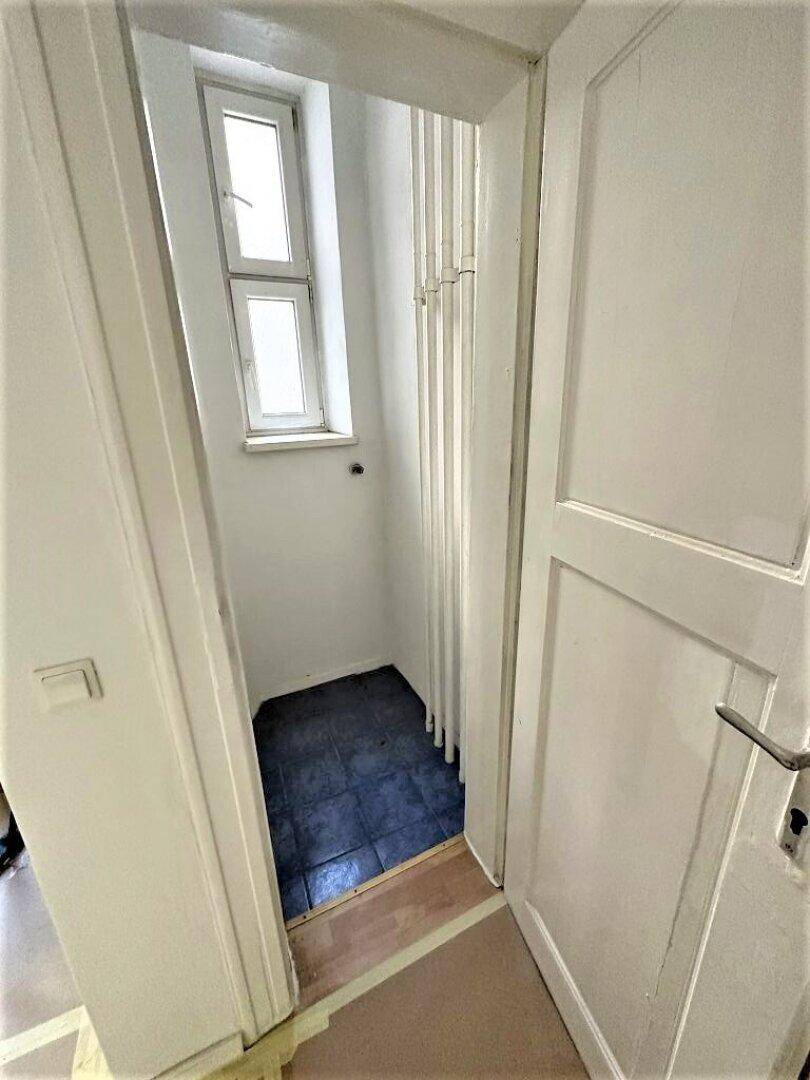 Kleiner Abstellraum mit Fenster und dunklem Fliesenboden, ideal für zusätzlichen Stauraum.